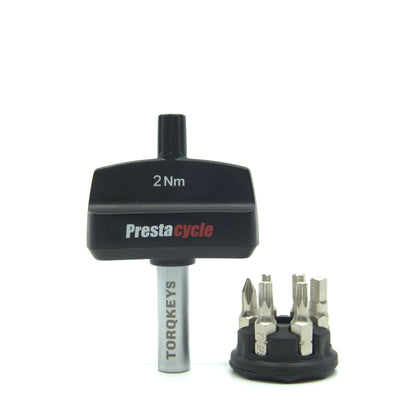 A Prestacycle Mini TorqKeys 2Nm preset torque tool stands upright beside its black holder containing six interchangeable bits, all displayed on a white background.