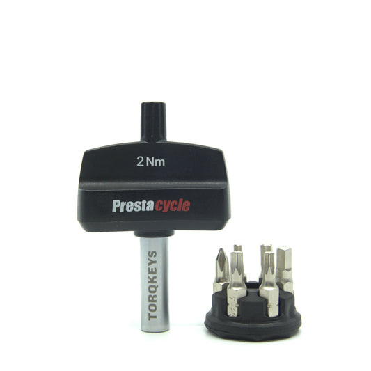 A Prestacycle Mini TorqKeys 2Nm preset torque tool stands upright beside its black holder containing six interchangeable bits, all displayed on a white background.