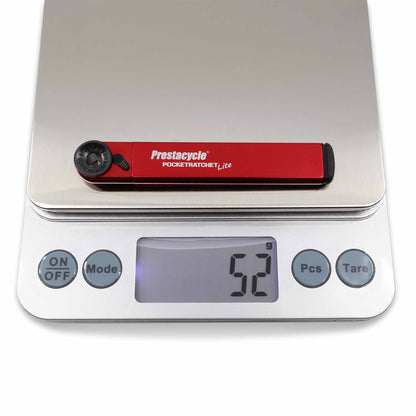 A Prestacycle PocketRatchet Lite multi-tool with bits stored in the handle sits on a digital kitchen scale, showing a weight of 52 grams.