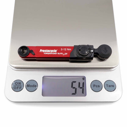 The Prestacycle TorqRatchet ELITE Lite, a red portable 2~12Nm torque multi-tool ratchet, sits on a digital scale reading 54 grams. The scale has multiple buttons and a clear LCD screen.